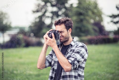 Young attractive man, a photographer, taking photographs in an urban area with an analog SLR camera photo