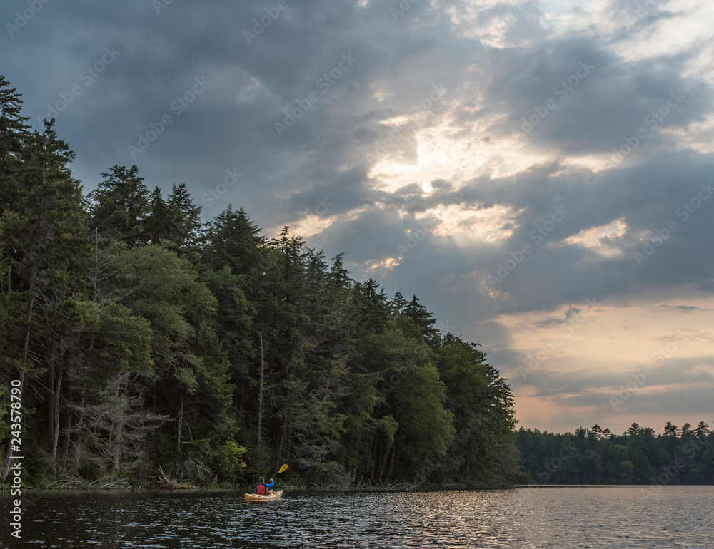 a woman enjoying a paddle on a quiet water lake with the sun peaking through the clouds