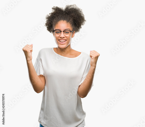 Young afro american woman wearing glasses over isolated background celebrating surprised and amazed for success with arms raised and open eyes. Winner concept.