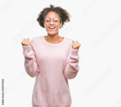 Young afro american woman wearing glasses over isolated background celebrating surprised and amazed for success with arms raised and open eyes. Winner concept.