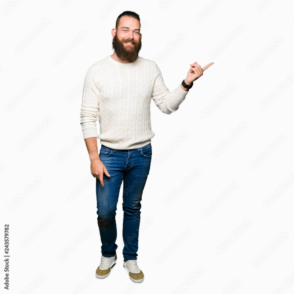 Young hipster man wearing winter sweater with a big smile on face, pointing with hand and finger to the side looking at the camera. Young hipster man wearing winter sweater with a big smile on face, pointing with hand and finger to the side looking at the camera.