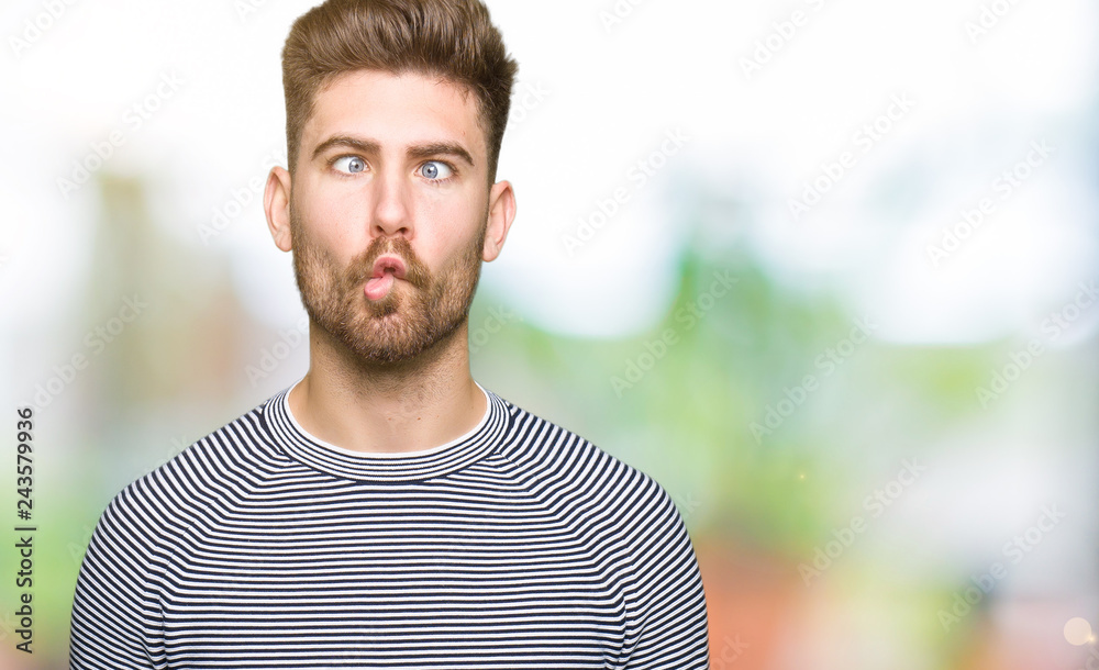 Young handsome man wearing stripes sweater making fish face with lips, crazy and comical gesture. Funny expression. Young handsome man wearing stripes sweater making fish face with lips, crazy and comical gesture. Funny expression.