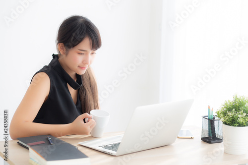 Beautiful young freelance asian woman smiling working and on laptop computer at desk office with professional, girl using notebook and drink coffee, business and lifestyle concept.