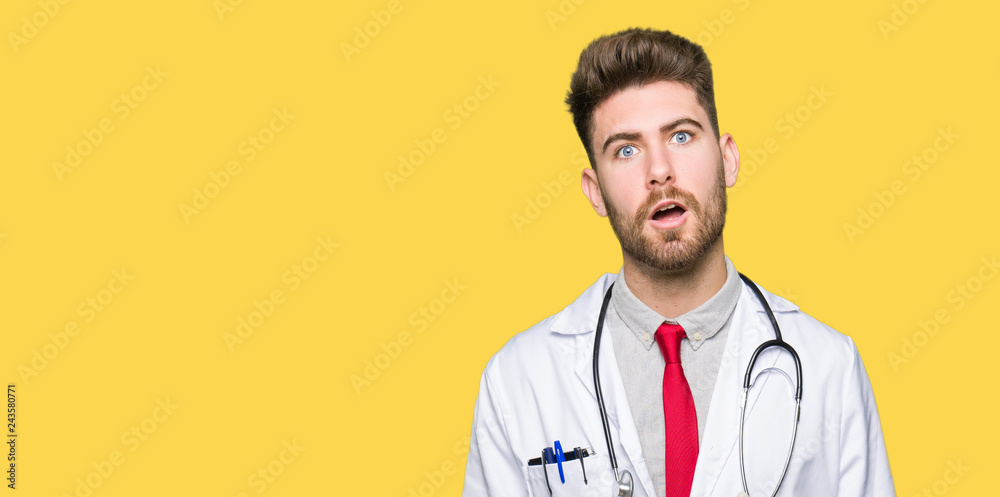Young handsome doctor man wearing medical coat In shock face, looking skeptical and sarcastic, surprised with open mouth Young handsome doctor man wearing medical coat In shock face, looking skeptical and sarcastic, surprised with open mouth