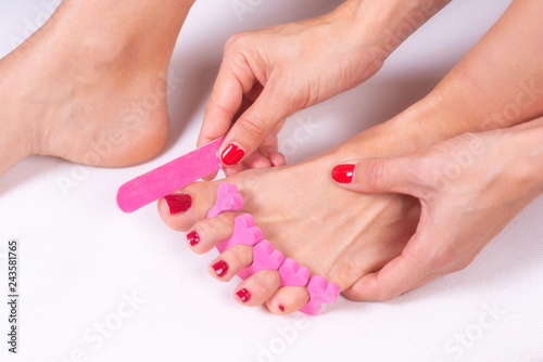 applying pedicure to woman s feet with red toenails  in pink toe separators .