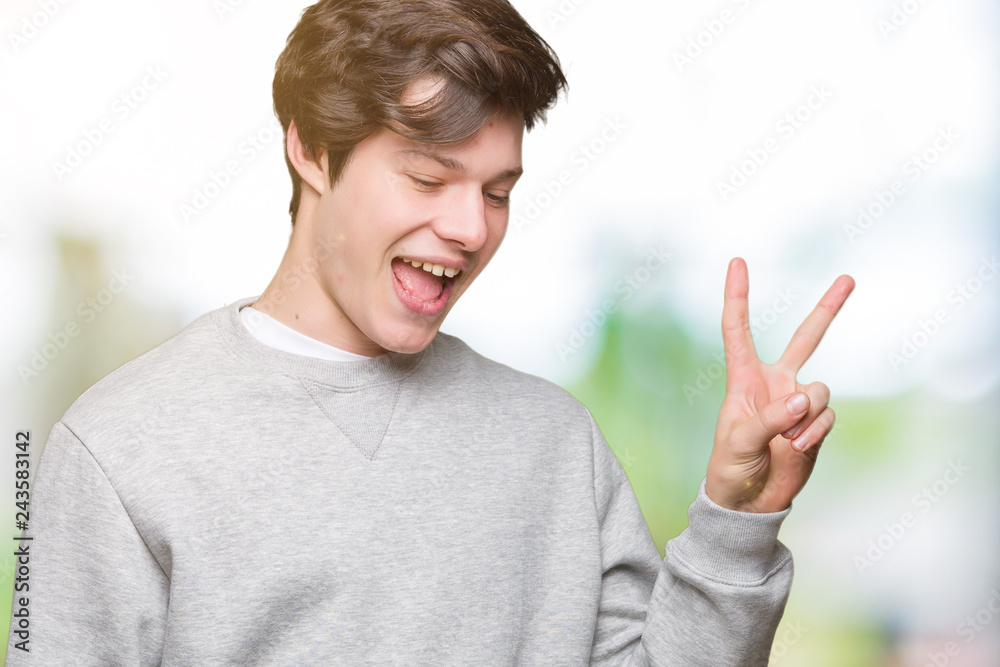 Young handsome sporty man wearing sweatshirt over isolated background smiling with happy face winking at the camera doing victory sign. Number two. Young handsome sporty man wearing sweatshirt over isolated background smiling with happy face winking at the camera doing victory sign. Number two.