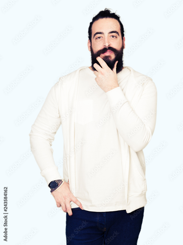 Fototapeta premium Young man with long hair and beard wearing sporty sweatshirt looking confident at the camera with smile with crossed arms and hand raised on chin. Thinking positive.