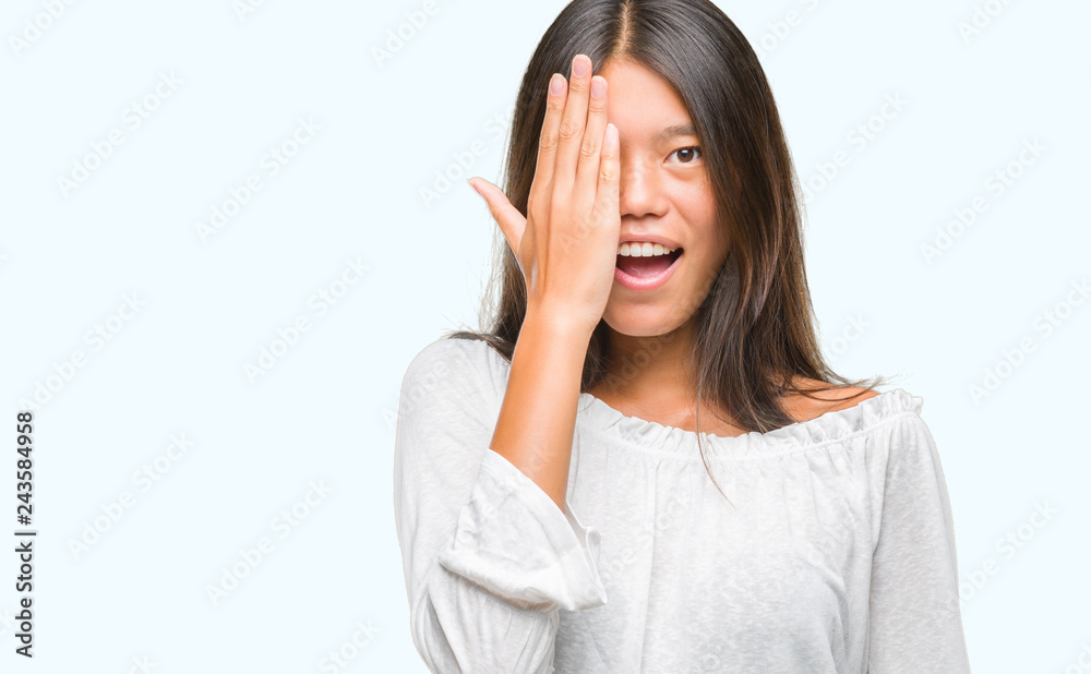 Young asian woman over isolated background covering one eye with hand with confident smile on face and surprise emotion. Young asian woman over isolated background covering one eye with hand with confident smile on face and surprise emotion.