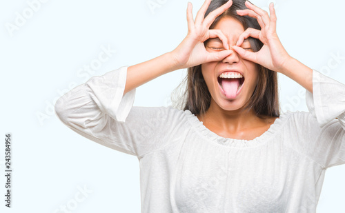 Young asian woman over isolated background doing ok gesture like binoculars sticking tongue out, eyes looking through fingers. Crazy expression.