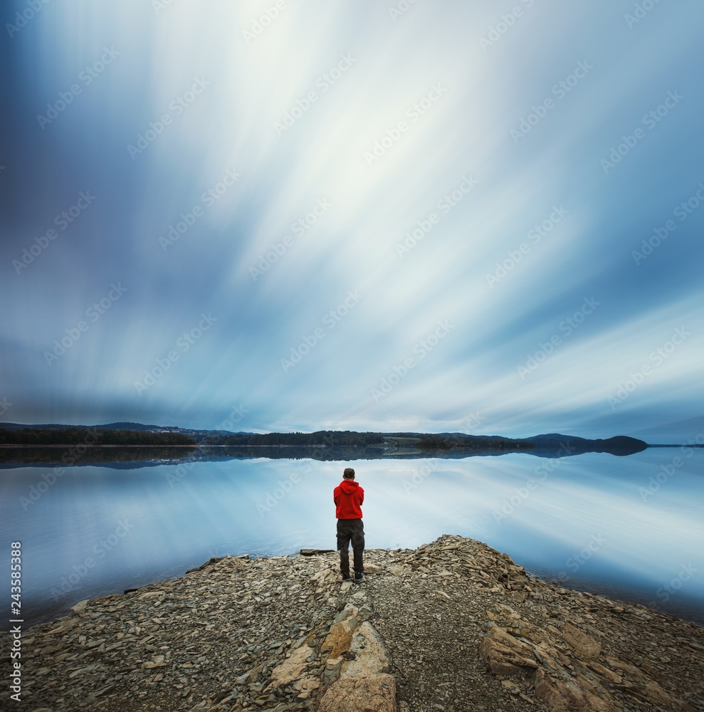 Surreal, dreamy landscape with man standing on rocky lake shore