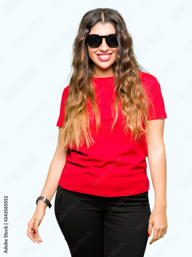 Fototapeta premium Young beautiful woman wearing red t-shirt and sunglasses with serious expression on face. Simple and natural looking at the camera.