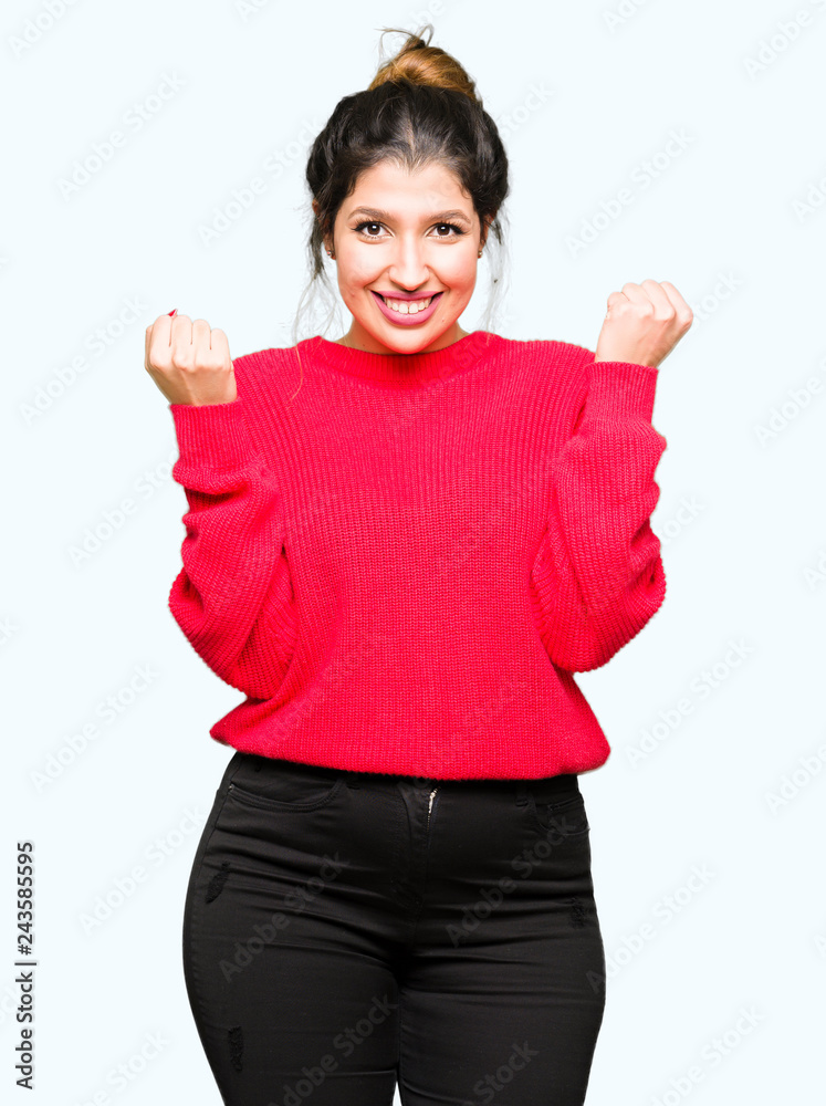 Young beautiful woman wearing red sweater and bun celebrating surprised and amazed for success with arms raised and open eyes. Winner concept. Young beautiful woman wearing red sweater and bun celebrating surprised and amazed for success with arms raised and open eyes. Winner concept.
