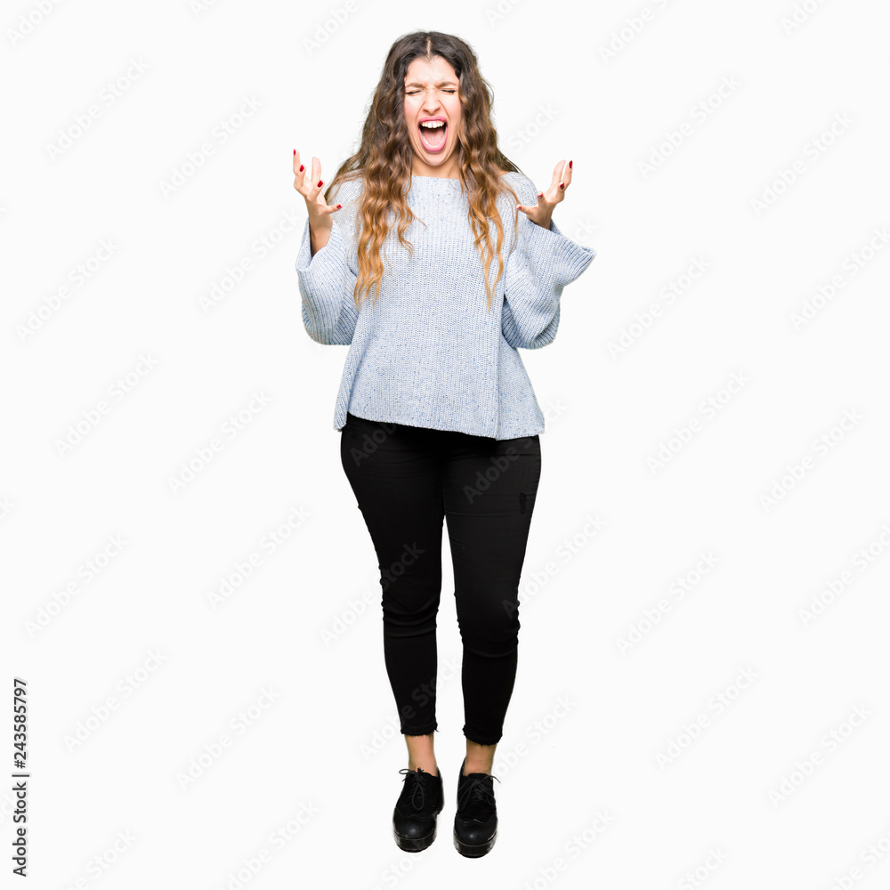 Young beautiful woman wearing winter sweater crazy and mad shouting and yelling with aggressive expression and arms raised. Frustration concept. Young beautiful woman wearing winter sweater crazy and mad shouting and yelling with aggressive expression and arms raised. Frustration concept.