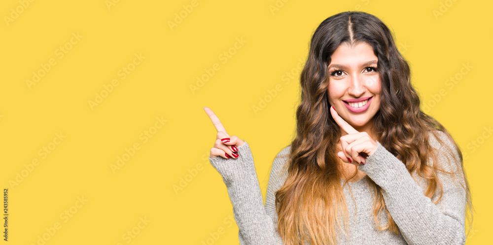 Fototapeta premium Young beautiful woman wearing winter dress smiling and looking at the camera pointing with two hands and fingers to the side.