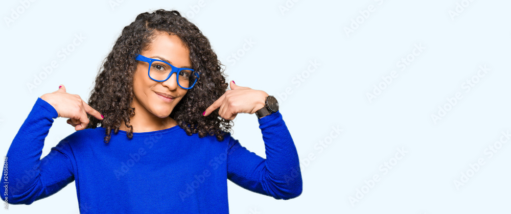 Fototapeta premium Young beautiful woman with curly hair wearing glasses looking confident with smile on face, pointing oneself with fingers proud and happy.