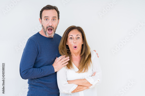 Beautiful middle age couple in love over isolated background afraid and shocked with surprise expression, fear and excited face.