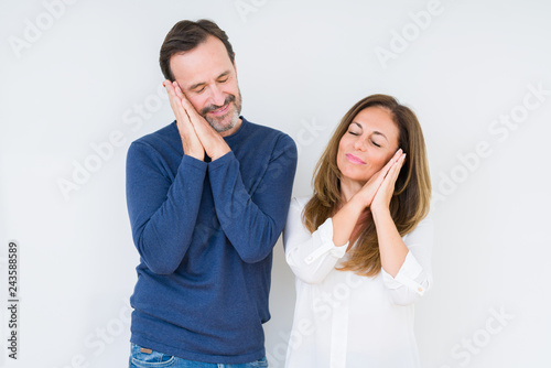 Beautiful middle age couple in love over isolated background sleeping tired dreaming and posing with hands together while smiling with closed eyes.