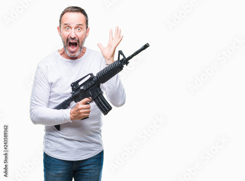 Middle age senior hoary criminal man holding gun weapon over isolated background very happy and excited, winner expression celebrating victory screaming with big smile and raised hands