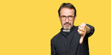 Middle age priest man wearing catholic robe looking unhappy and angry showing rejection and negative with thumbs down gesture. Bad expression.