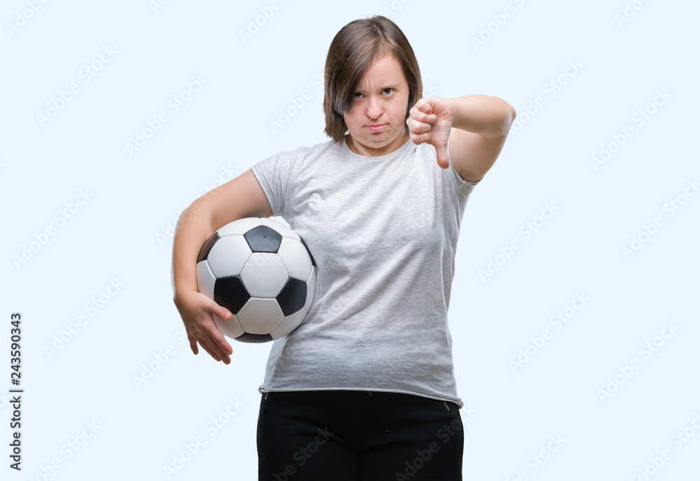 Young adult woman with down syndrome holding soccer football ball over isolated background with angry face, negative sign showing dislike with thumbs down, rejection concept