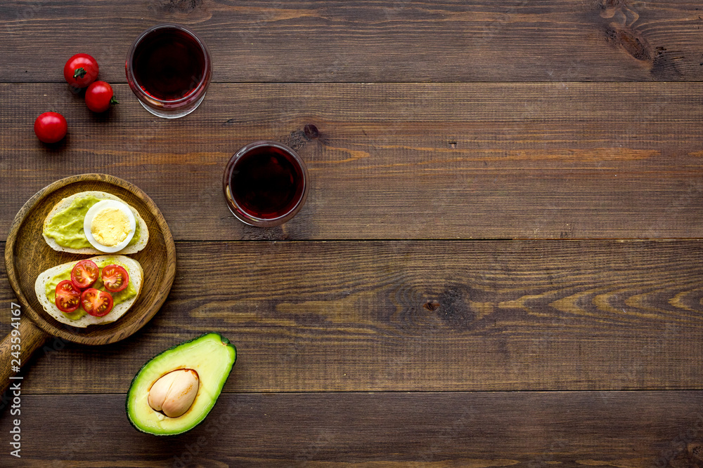 Light appetizer with avocado. Toasts with vegetables and guacamole near glasses of wine on dark wooden background top view space for text Light appetizer with avocado. Toasts with vegetables and guacamole near glasses of wine on dark wooden background top view space for text