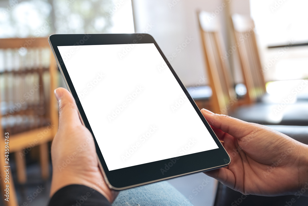 Mockup image of a woman holding black tablet pc with blank white screen while sitting in cafe