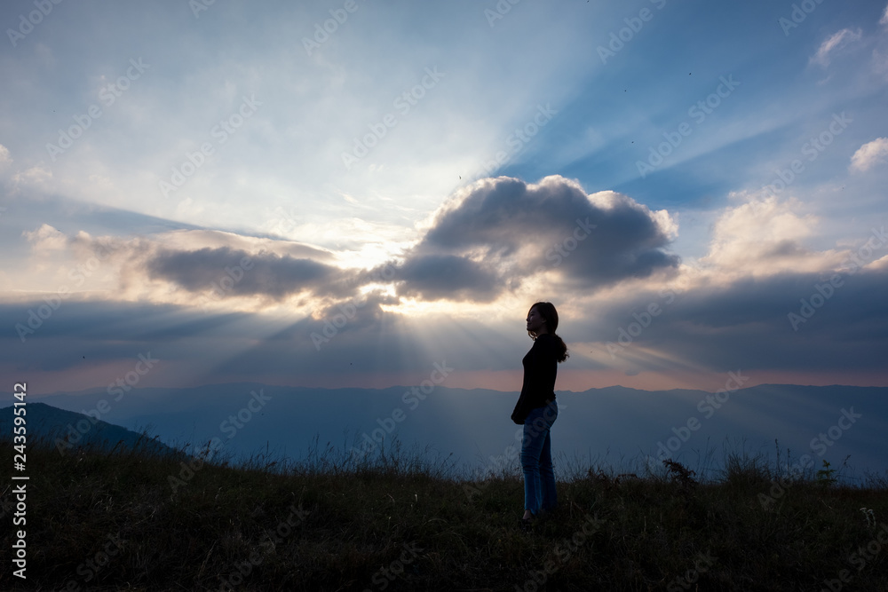 A woman standing and watching sunset with mountains view in the evening