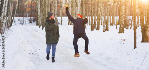 Two young modern man while walking through a birch forest in winter. One of them slipped and lost his balance, his friend held out his arms. Freeze frame before falling into the snow. © raisondtre