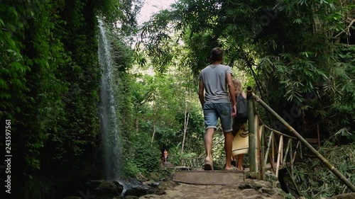 A couple of tourists walking on the bridge with bamboo railing and approaching wonderful waterfall near Ubud, Bali, Indonesia. photo