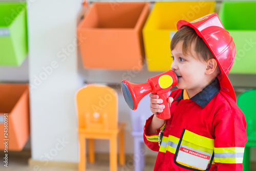 Slika na platnu Caucasian boy kid dress up to fireman and use speaker at roll play classroom,Kindergarten preschool education concept