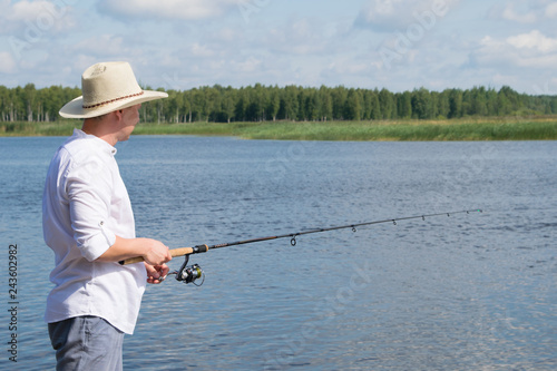 a man in a hat, outdoors, engaged in fishing on the pond