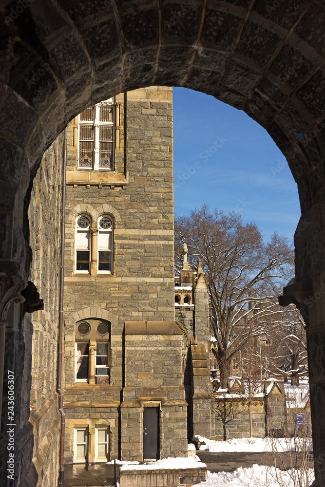 Main wing profile of Healy Hall building framed by its porch arch in Georgetown suburb of Washington DC. Intricate stained-glass patterns in windows of the building and wintery panorama outside.