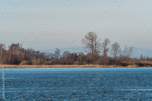 river reflecting the blue sky with small island with trees and mountain range in the background on a hazy day