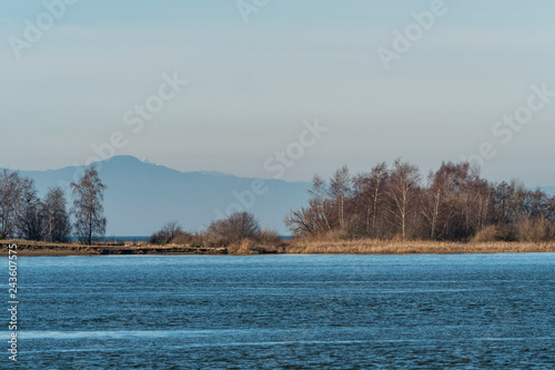 river reflecting the blue sky with small island with trees and mountain range in the background on a hazy day
