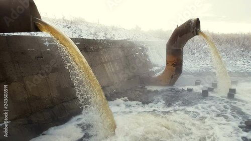 Wastewater from two large rusty pipes merge into the river in clouds of steam