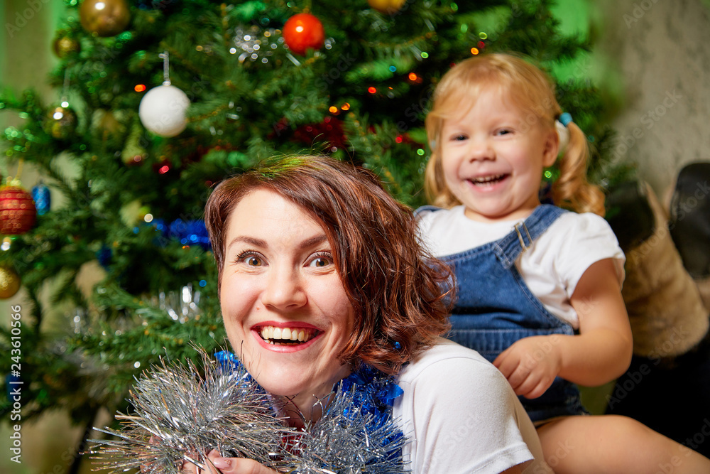 Nice mother and her cute daughter near Christmas tree in the room