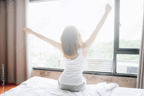 Back view of woman stretching in bed after waking up in the morning, start a new day with happiness.