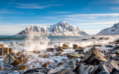 Arctic ocean wave hitting rocks with sunshine mountain