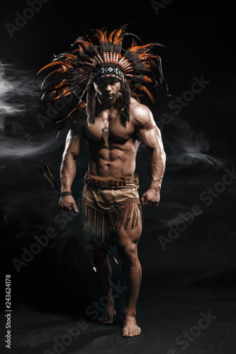 Dekoracja na wymiar  american-indian-apache-warrior-chief-in-traditional-clothing-and-feathered-headdress-with-weapon-indian-chieftain-of-the-tribe-with-muscled-strength-body-on-smoke-dark-background
