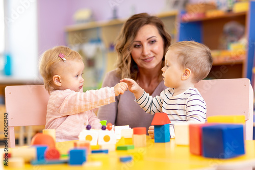 Nursery teacher looking after children in nursery. Little kids toddlers girl and boy play together with toys.