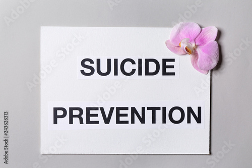 Paper sheet with text SUICIDE PREVENTION and flower on light background