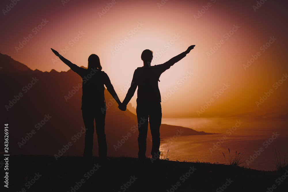 Silhouettes of happy couple enjoy travel at sunset mountains at sea