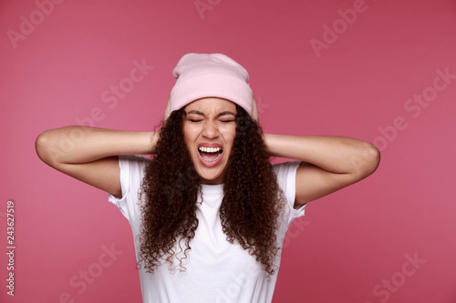 African woman covering ears with her hands, over a pink background