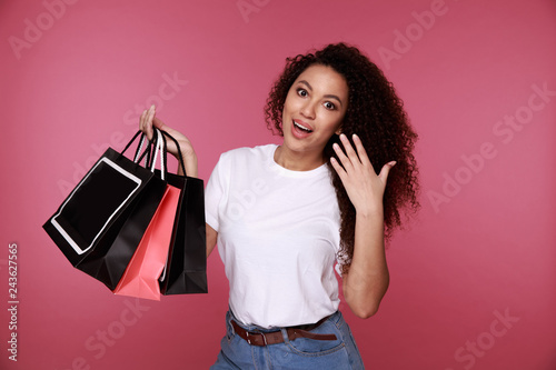 Portrait of an excited young african woman holding shopping bags and showing credit card isolated over pink background