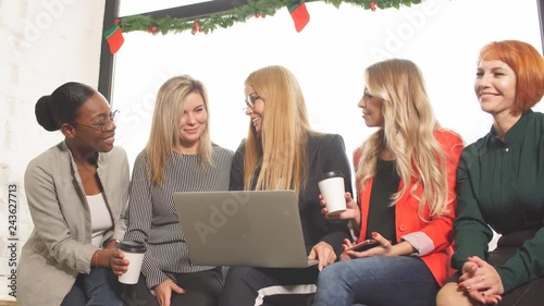 Group of designers working on a project as a team, diverse women gathered together near laptop of red-haired female colleague. photo