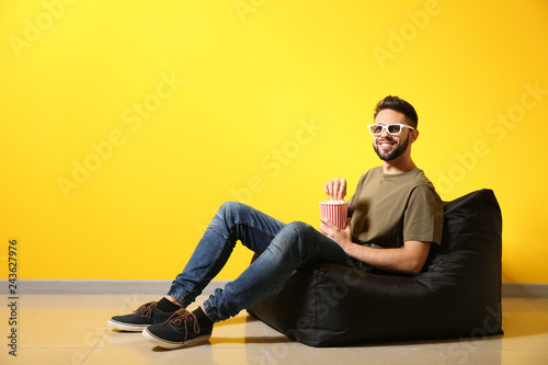 Young man with popcorn watching movie while sitting near color wall