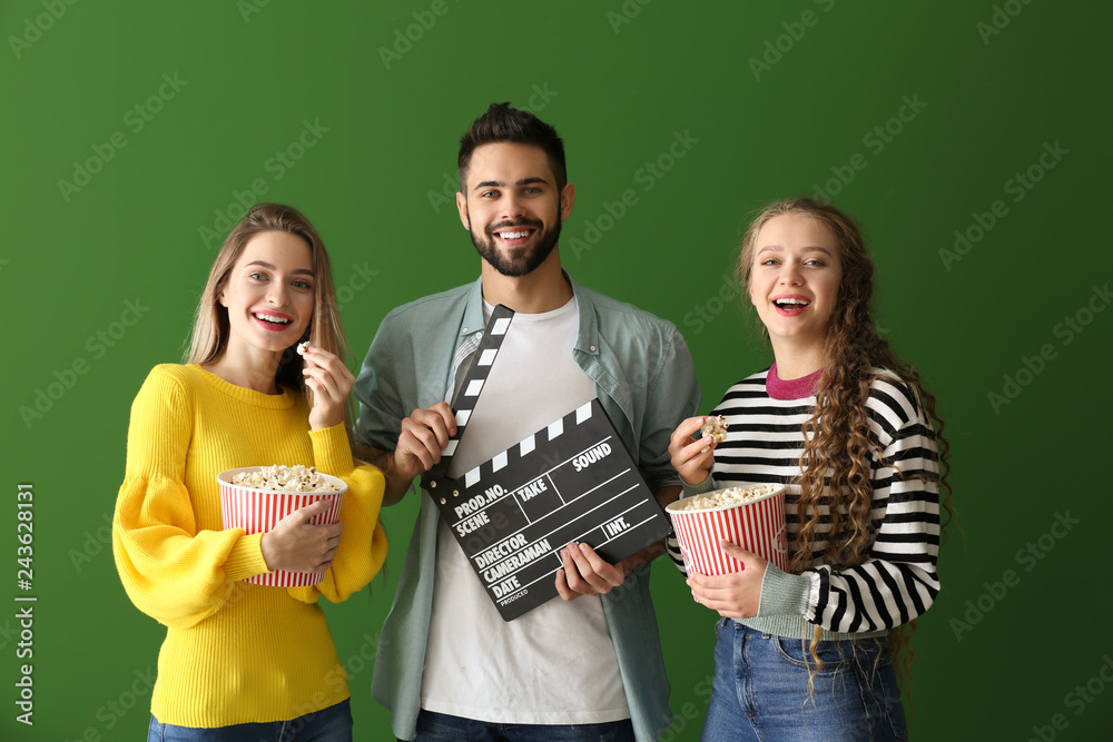 Young people with popcorn and movie clapper on color background