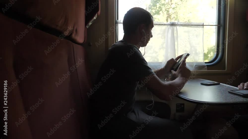 silhouette of a man on a train railway car listening to music on headphones writing a message in a messenger social media smartphone. slow motion lifestyle video travel by train . man with smartphones