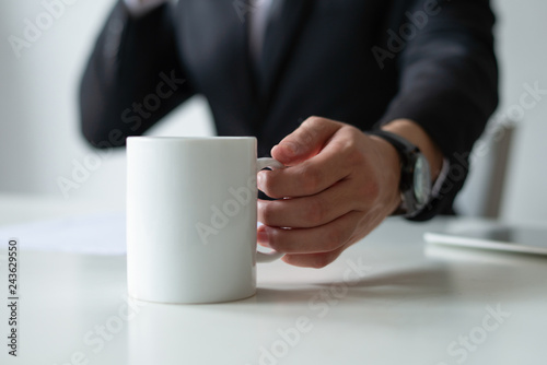 Closeup of business man drinking tea at workplace. Entrepreneur wearing suit and working at desk. Office occupation and workplace concept. Cropped view.