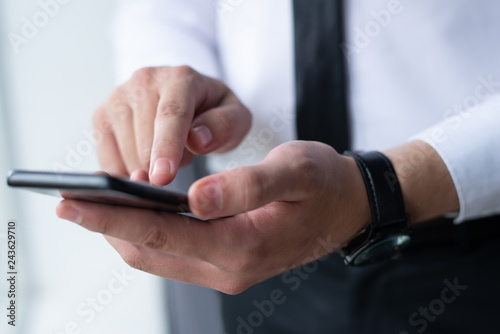 Closeup of business man networking on smartphone. Entrepreneur holding and using digital device. Communication and technologies in business concept. Cropped view.